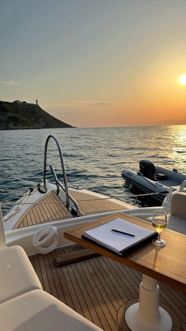 A boat deck at sunset with a glass of white wine and an open notebook.